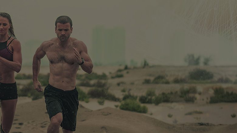 Two people running on a sandy terrain.