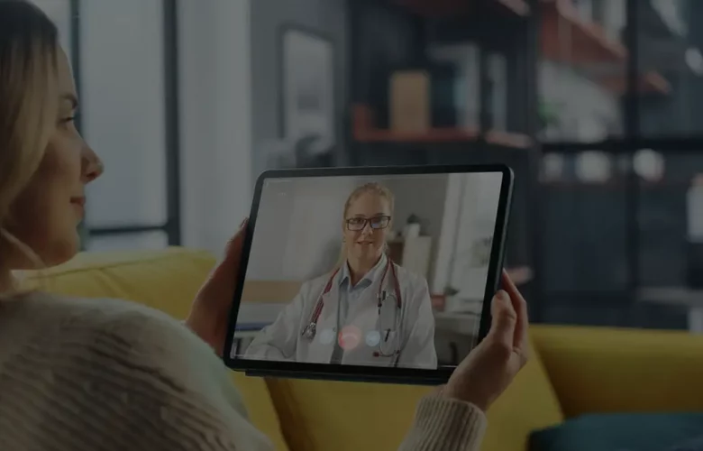 Woman on couch having a video call with a doctor on a tablet.