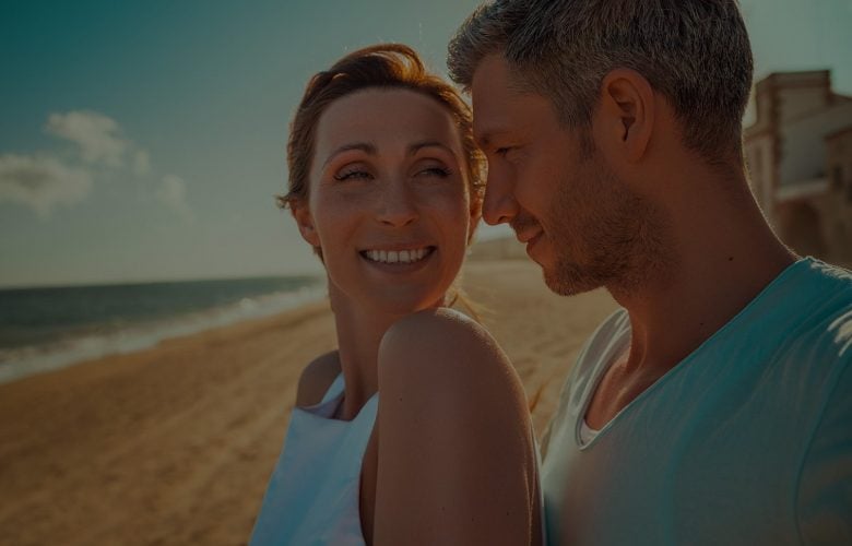 Couple smiling on a sunny beach.